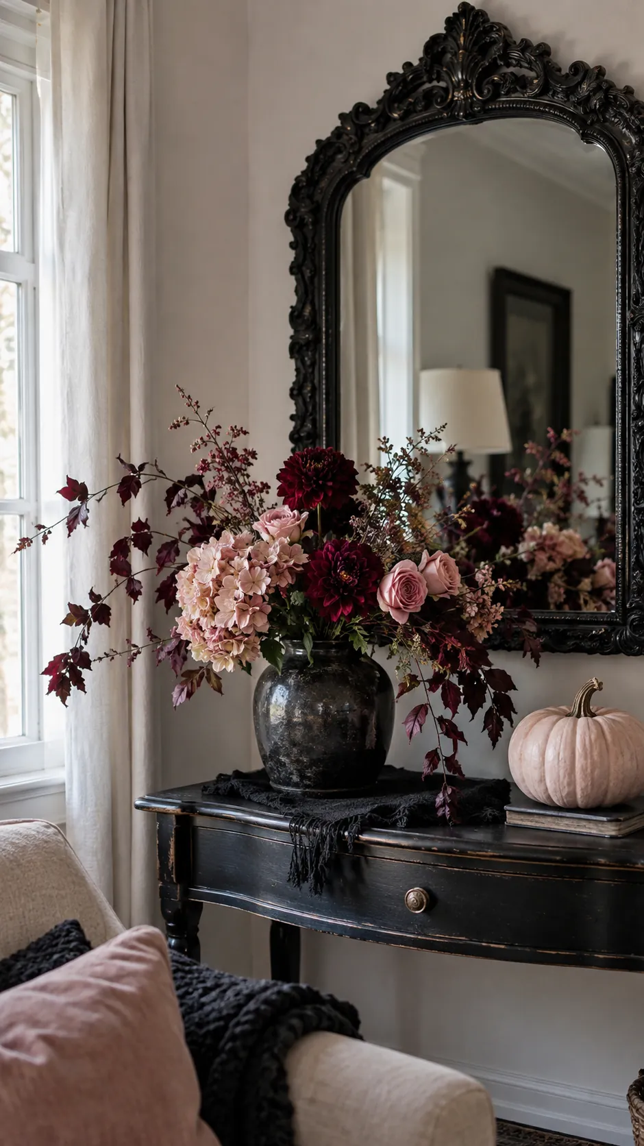 Pink and black Halloween decor with a low arrangement of blush and deep burgundy flowers set in front of the mirror