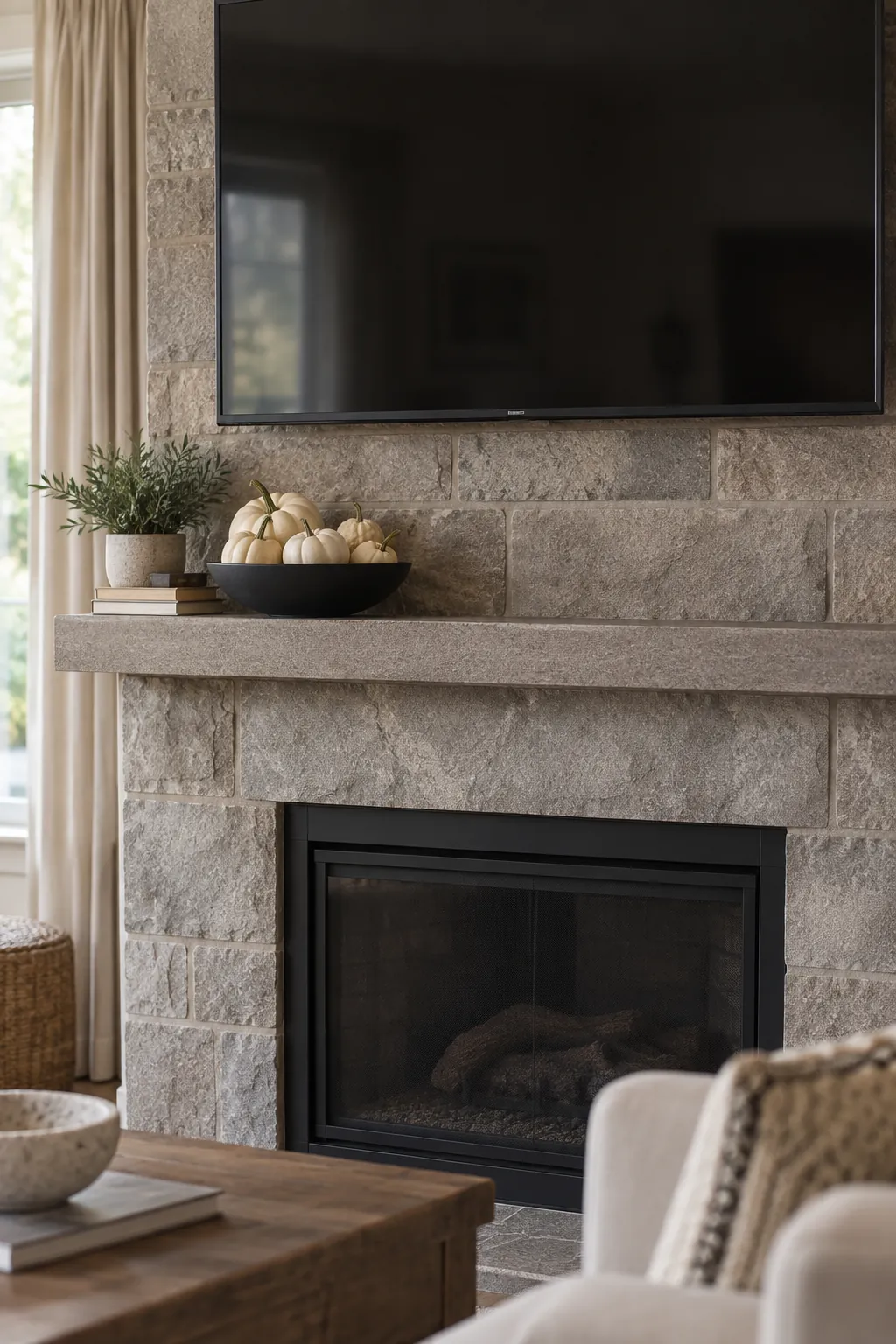White mini gourds in a shallow black bowl beneath a wall mounted TV