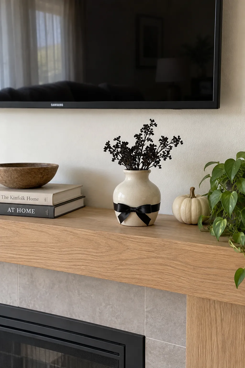 Low vase wrapped with black ribbon on a Halloween mantel below a television