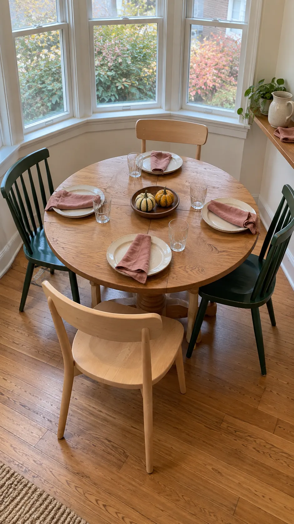 Two pale wooden chairs and two dark dining chairs arranged alternately around a small Thanksgiving table