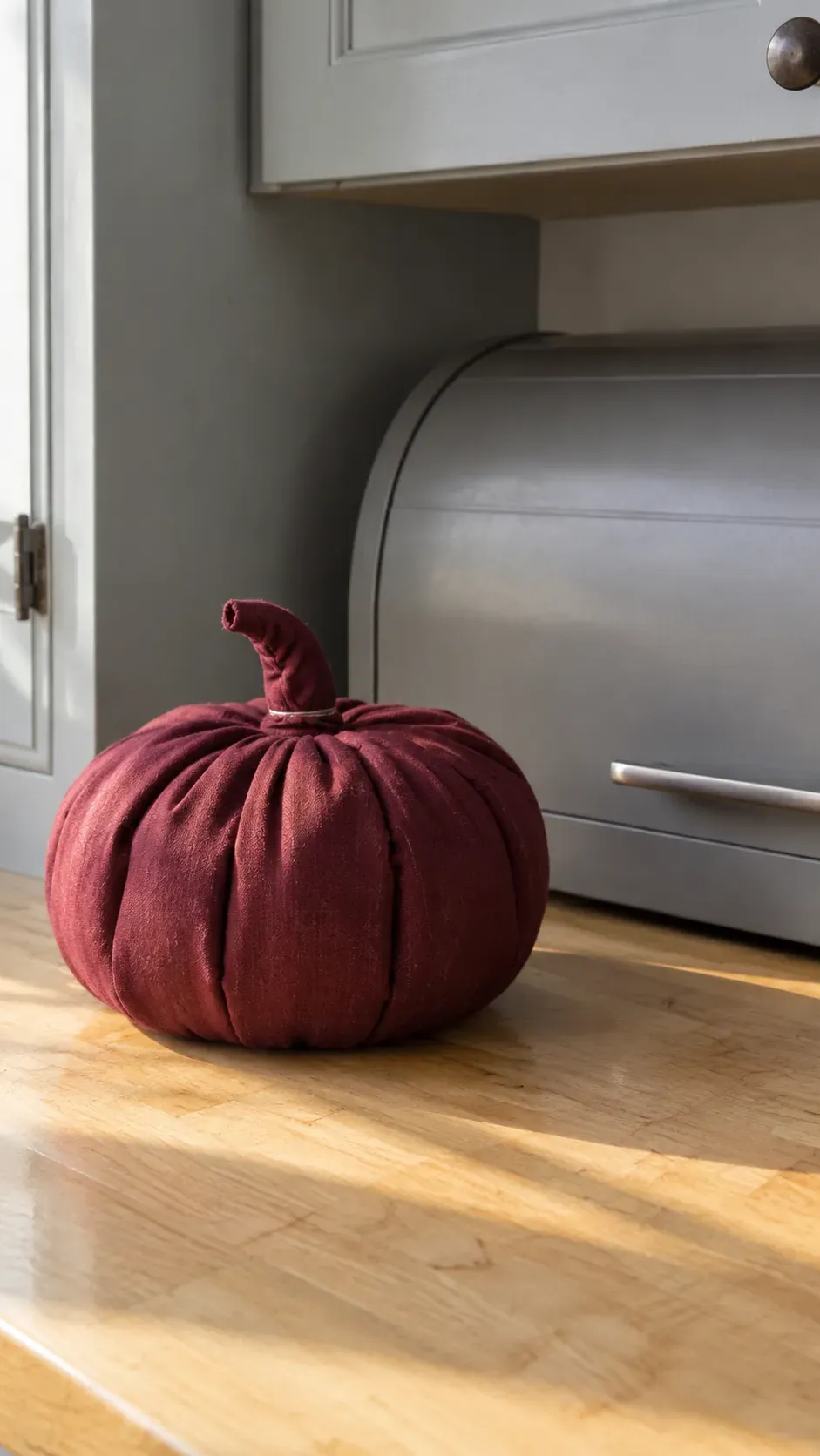 A handmade muted burgundy fabric pumpkin beside a painted bread box