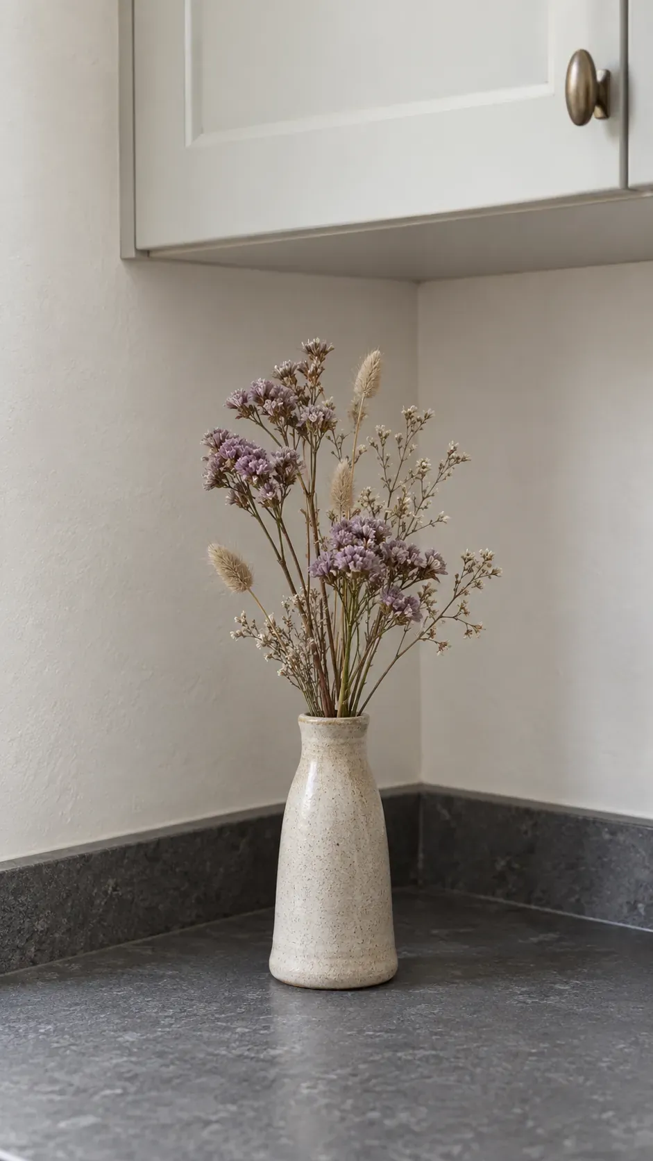 A narrow weighted vase with a small dried flower bouquet in a quiet kitchen corner
