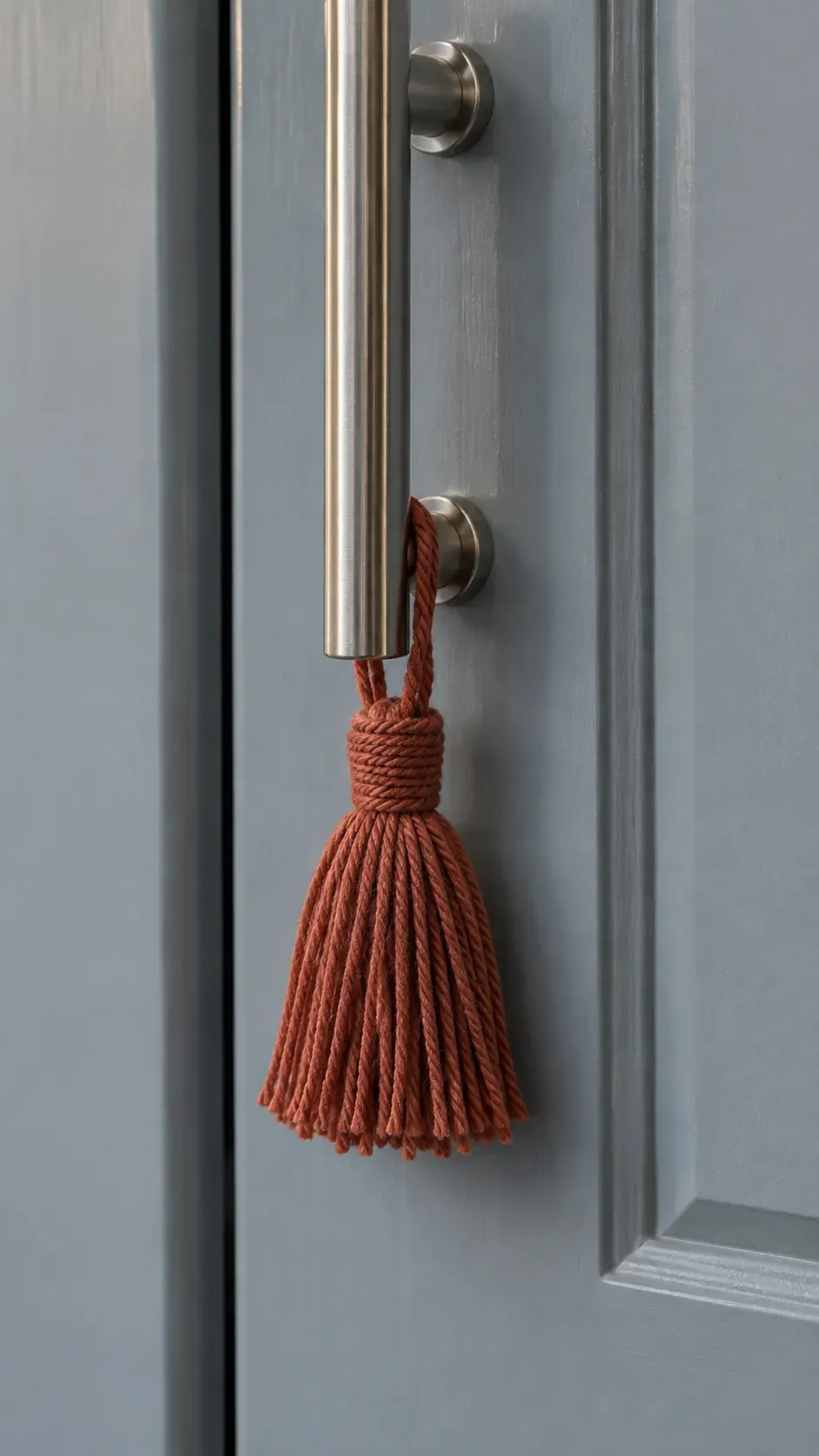 A short dark terracotta cotton tassel on a pantry cabinet handle away from cooking appliances