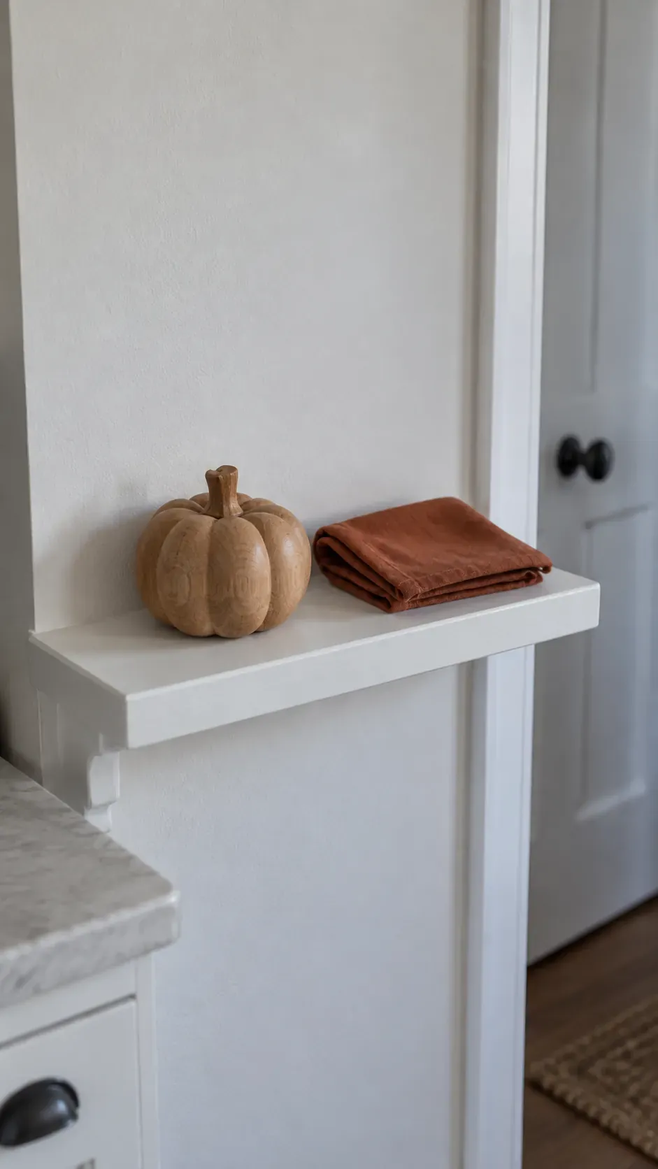 One small wooden pumpkin and a folded russet fabric swatch on a narrow secure kitchen ledge