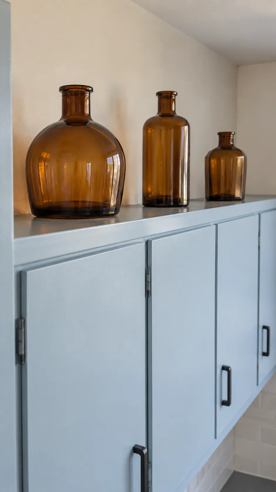 Three empty amber glass bottles spaced above pale blue kitchen cabinets