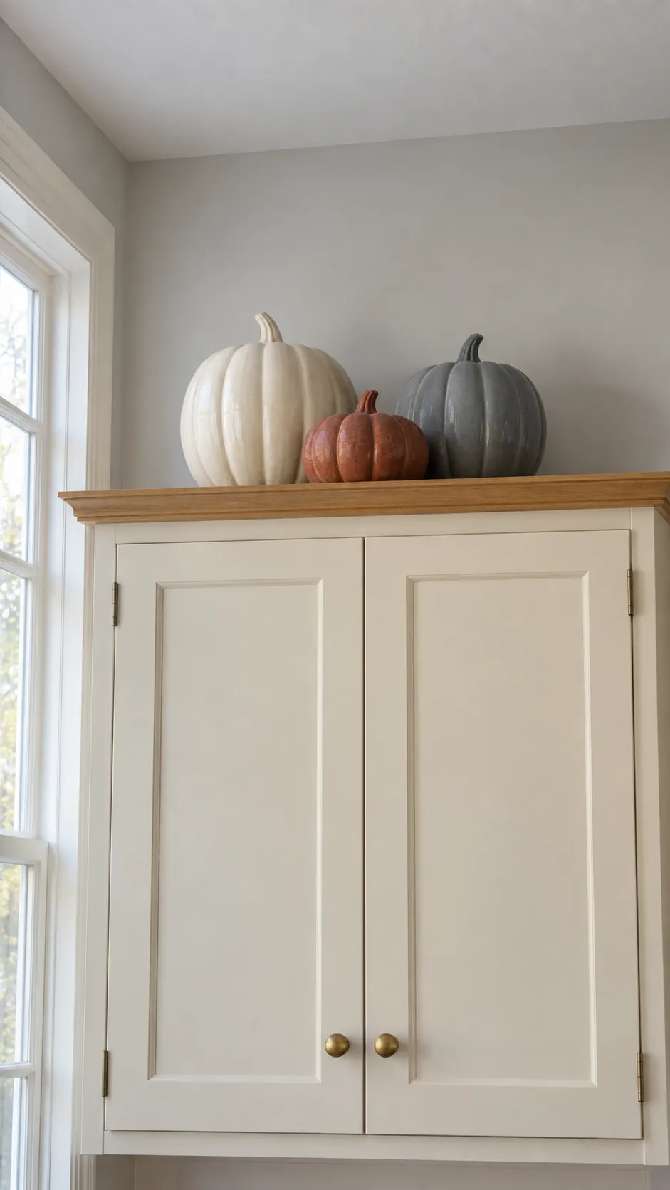 Three matte ceramic pumpkins grouped above cream kitchen cabinets with open space around them