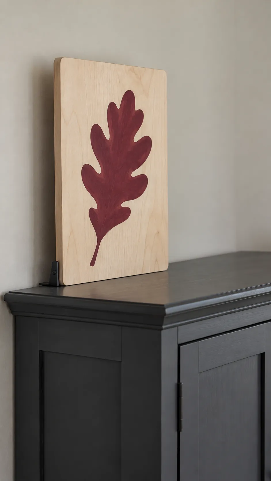 A securely supported lightweight wood panel with a burgundy oak leaf silhouette above kitchen cabinets
