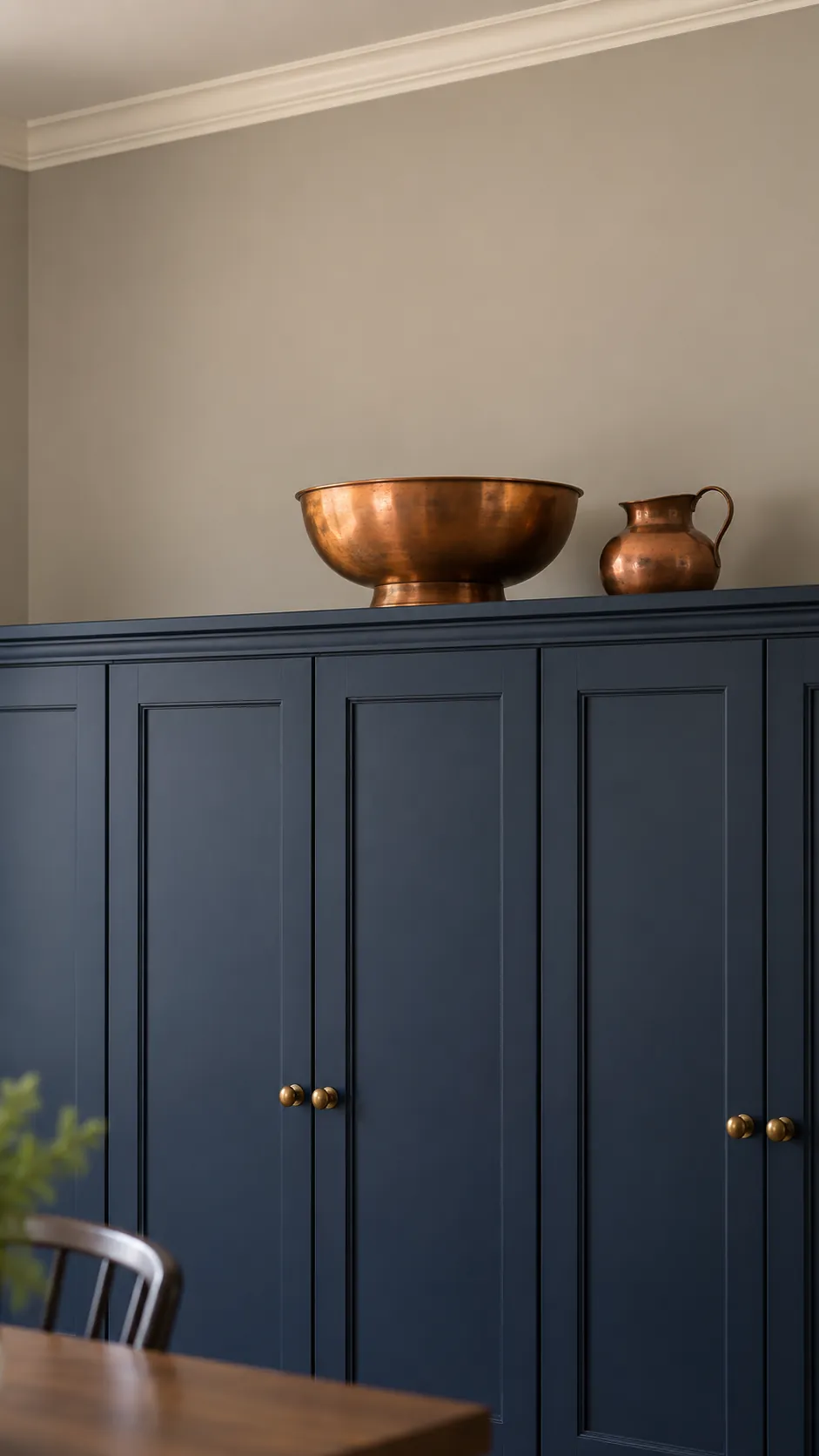 A compact group of a copper bowl and small copper vessel on the top of dark kitchen cabinets
