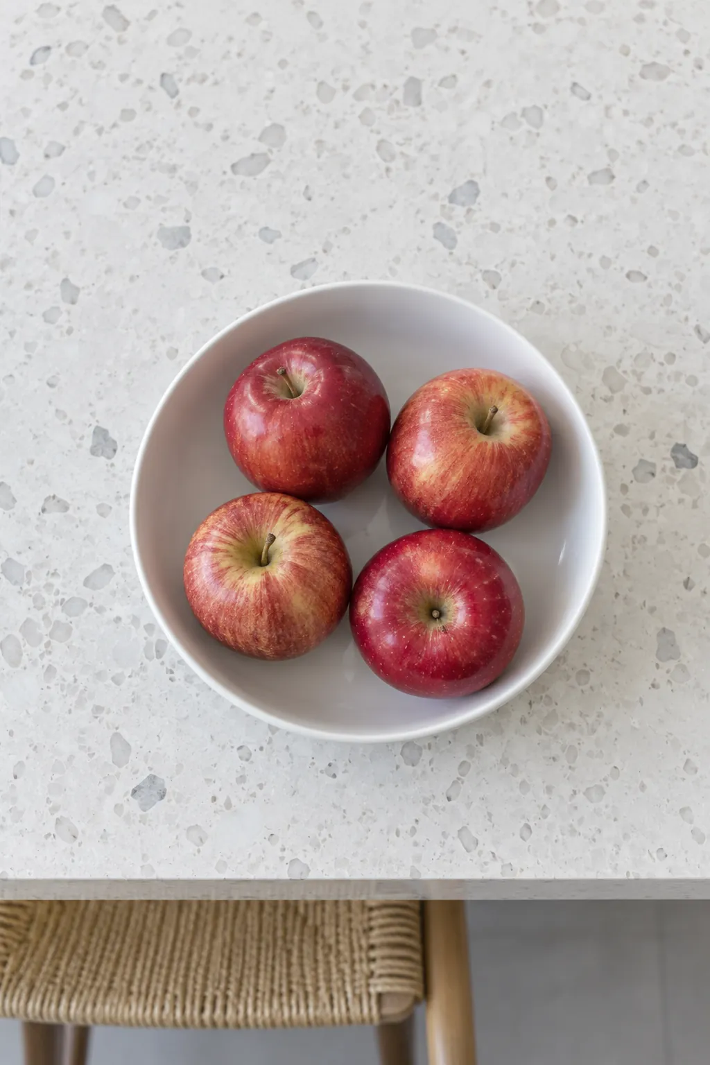 A shallow white serving bowl with red apples on a modern island