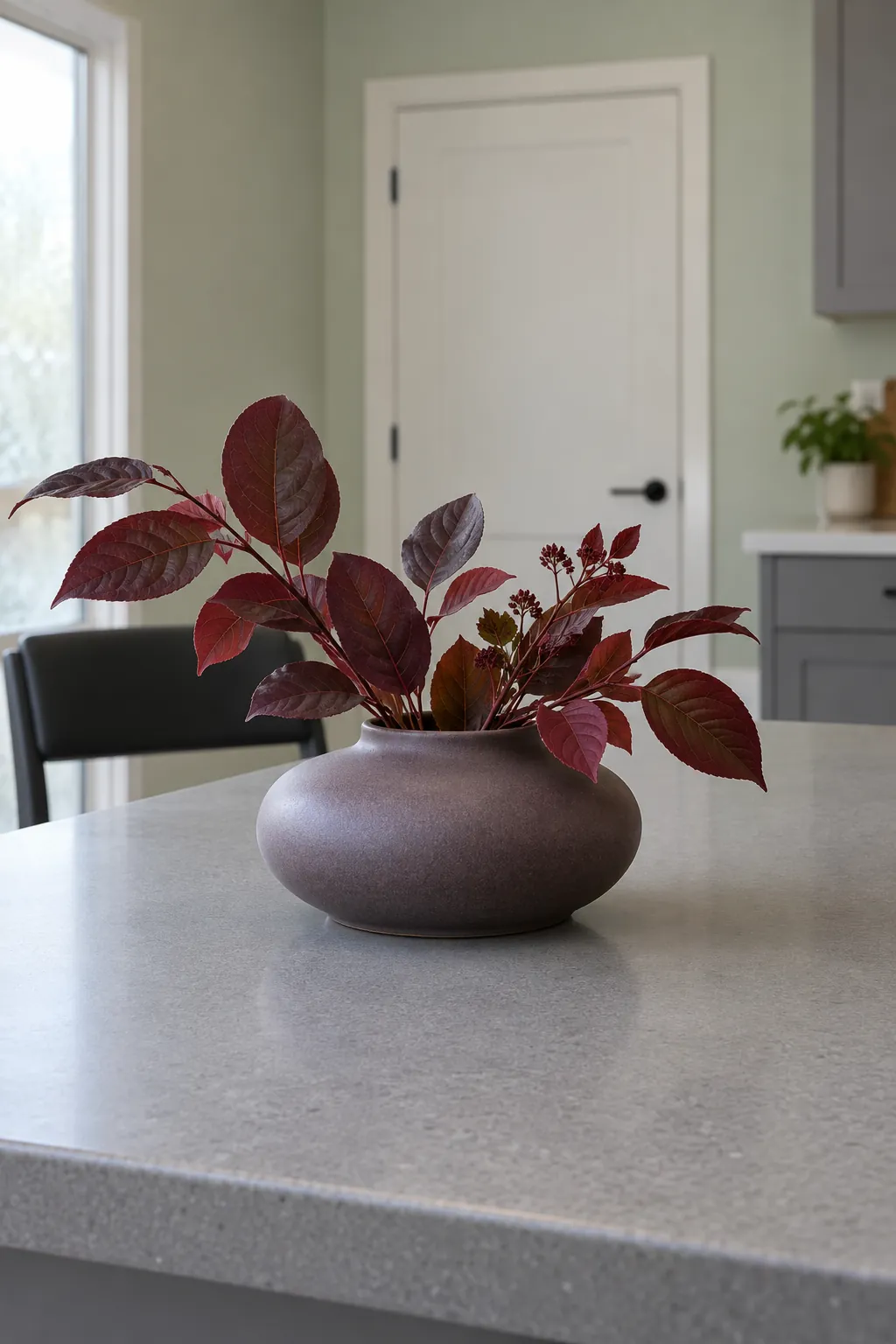 A low wide vase of short plum foliage at the seating end of a kitchen island