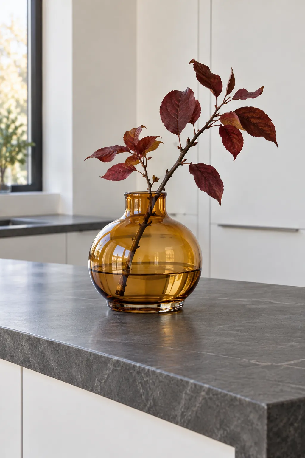 A broad amber vase with one restrained autumn branch set back from a kitchen island edge