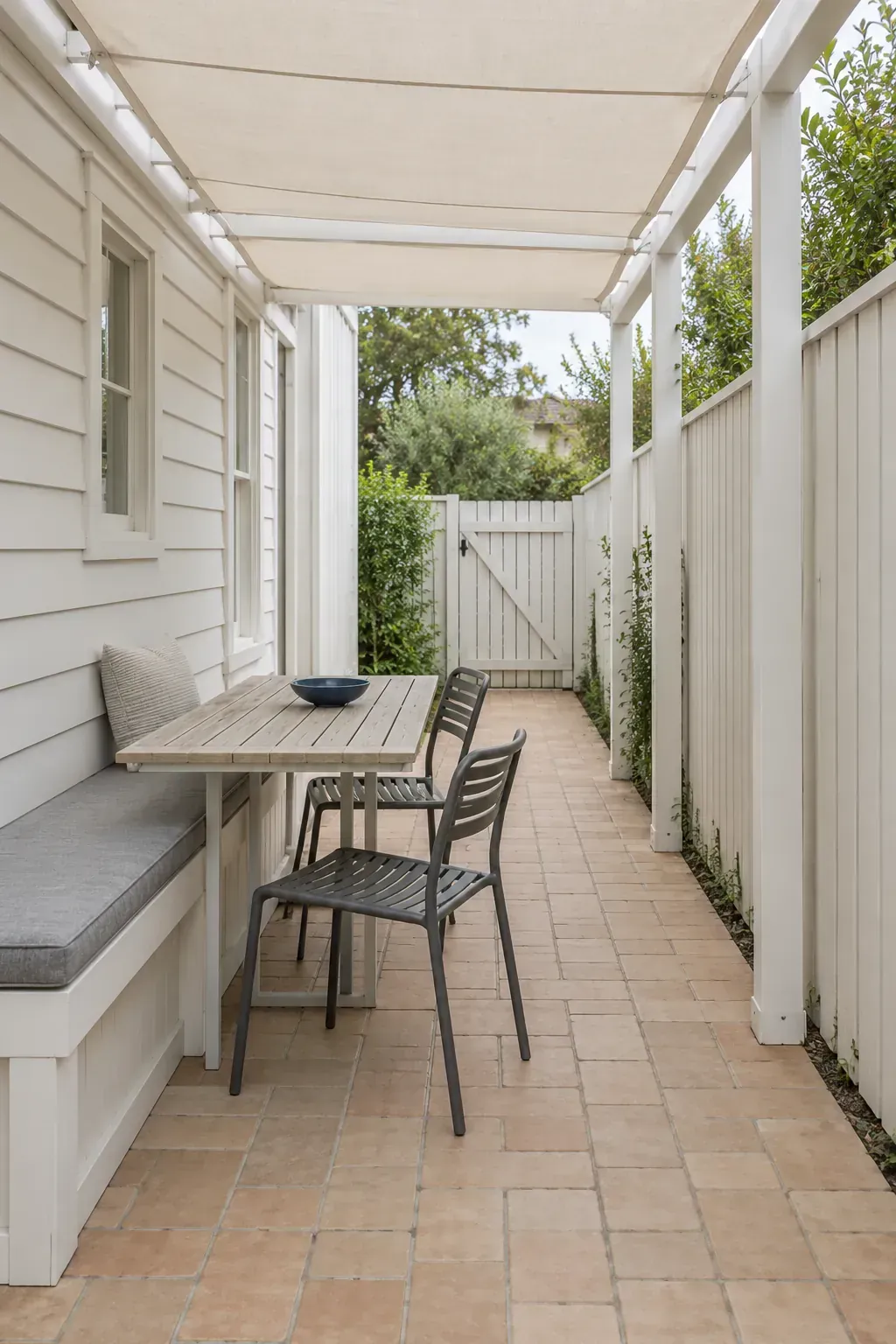 A narrow patio with furniture in a line beneath a patio pergola