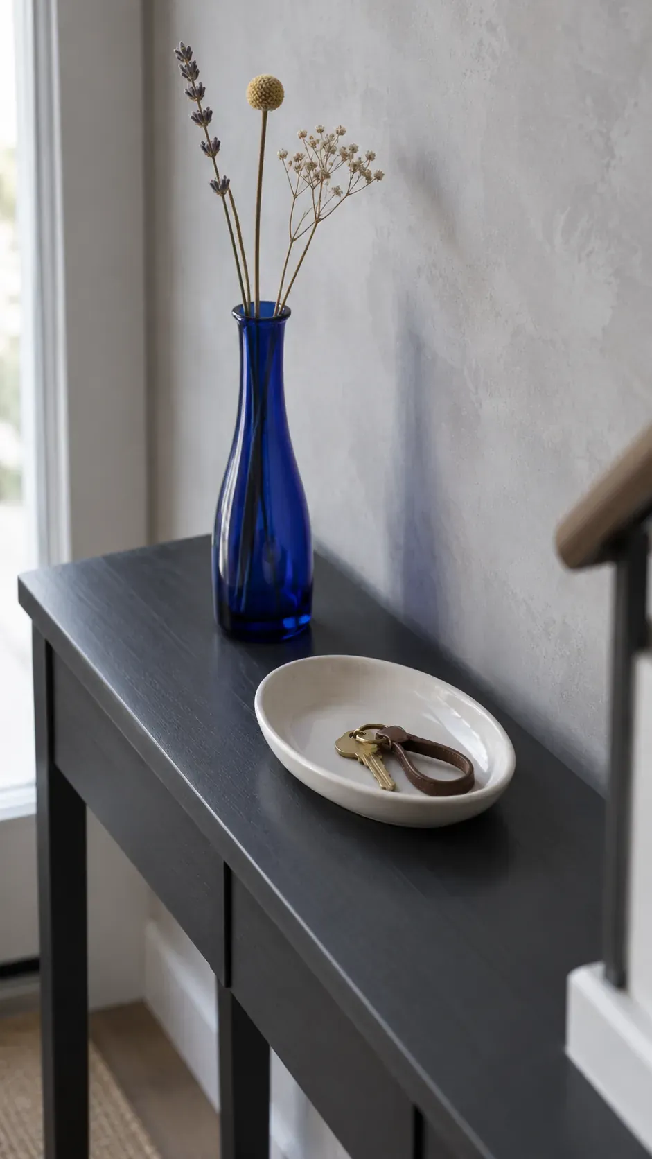 A Tall Vase Behind a Low Key Dish on an entryway console with accessible keys