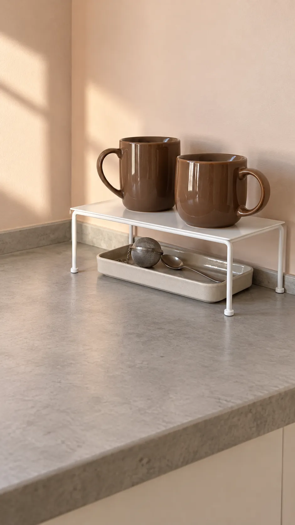 Compact countertop riser separating mugs from a small tray in a small rental kitchen