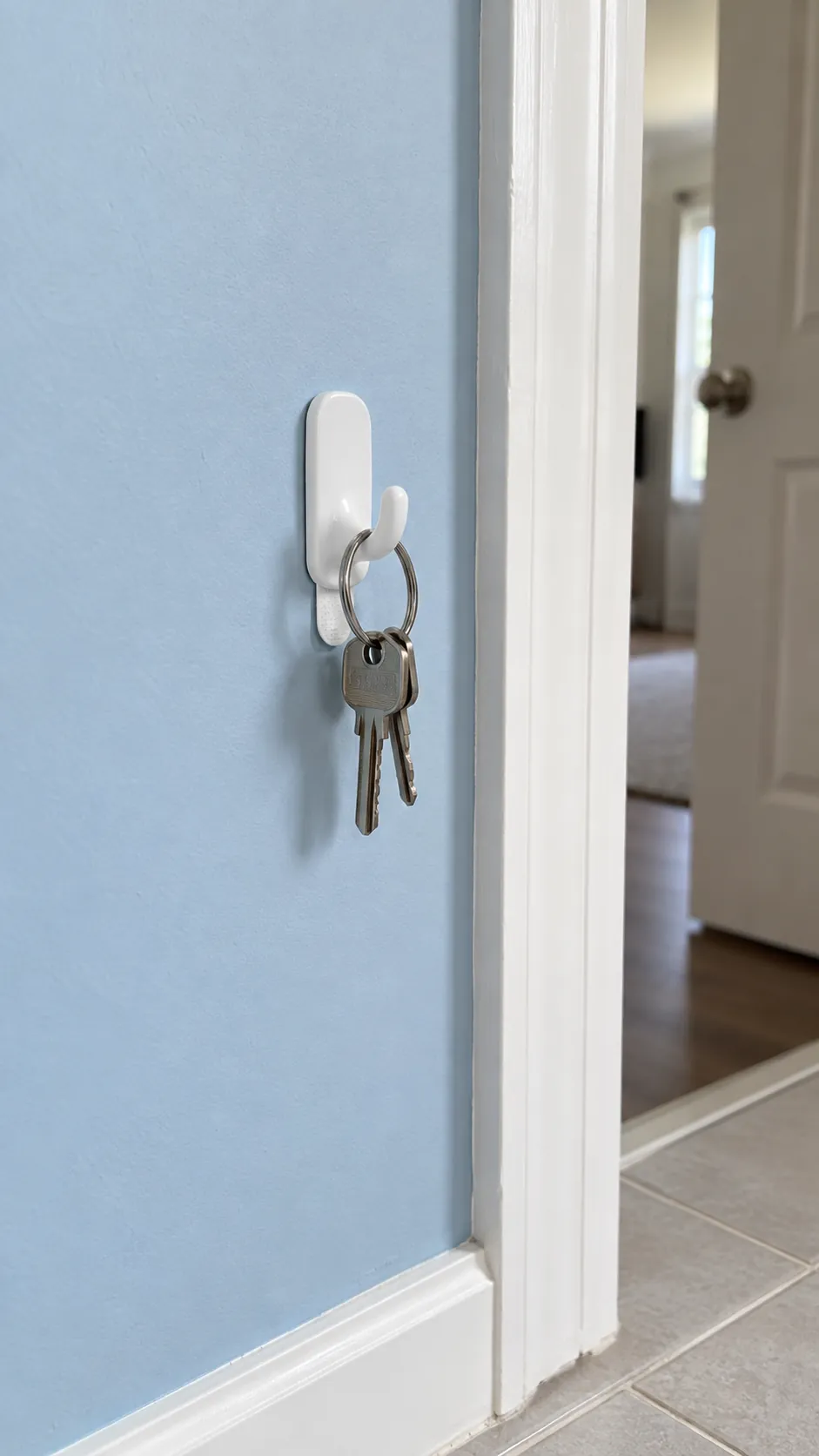 Small removable hook holding a light key ring on a smooth painted surface