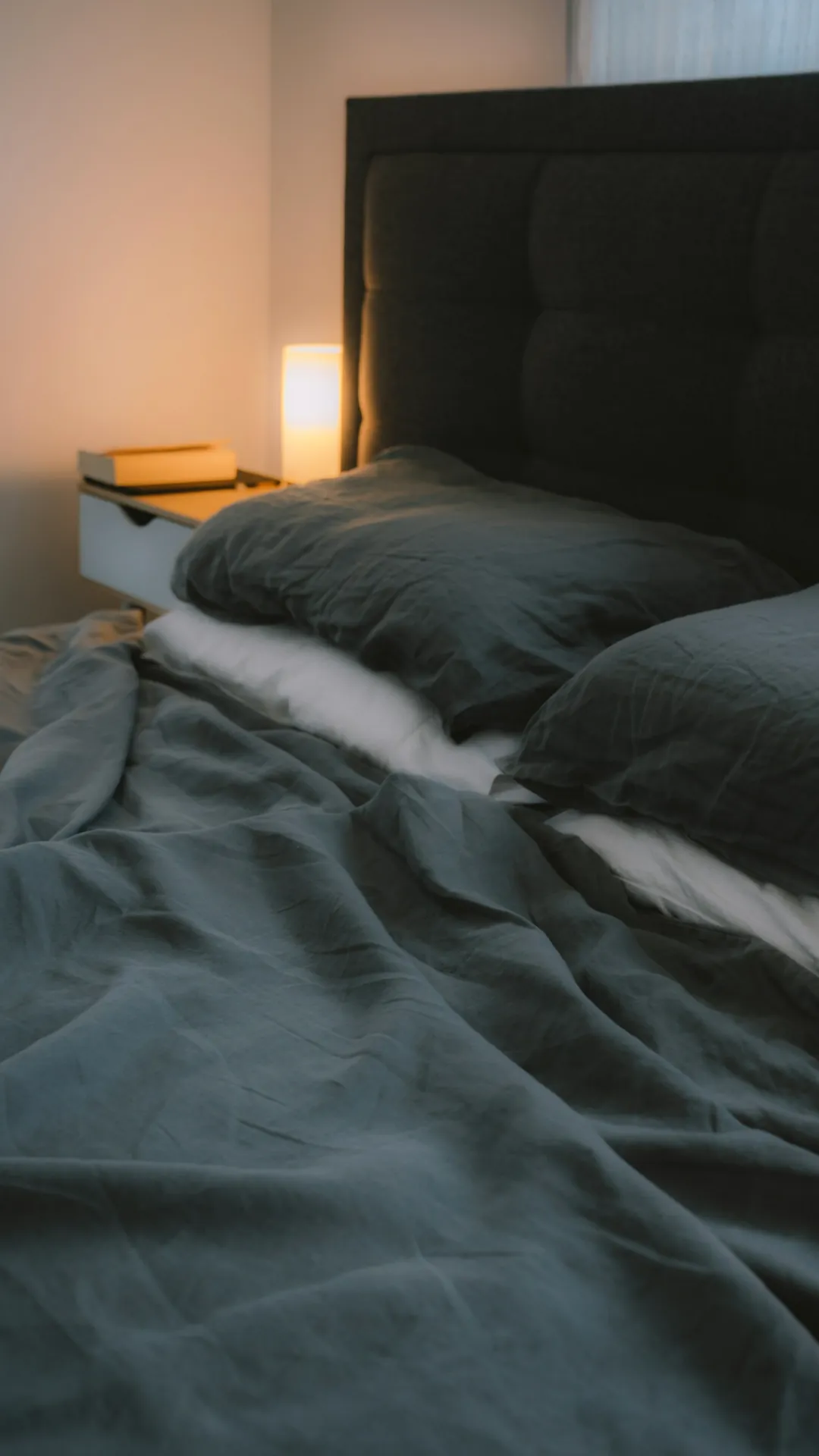 Cozy bedtime reading spot lit by a warm bedside lamp with the main ceiling light turned off