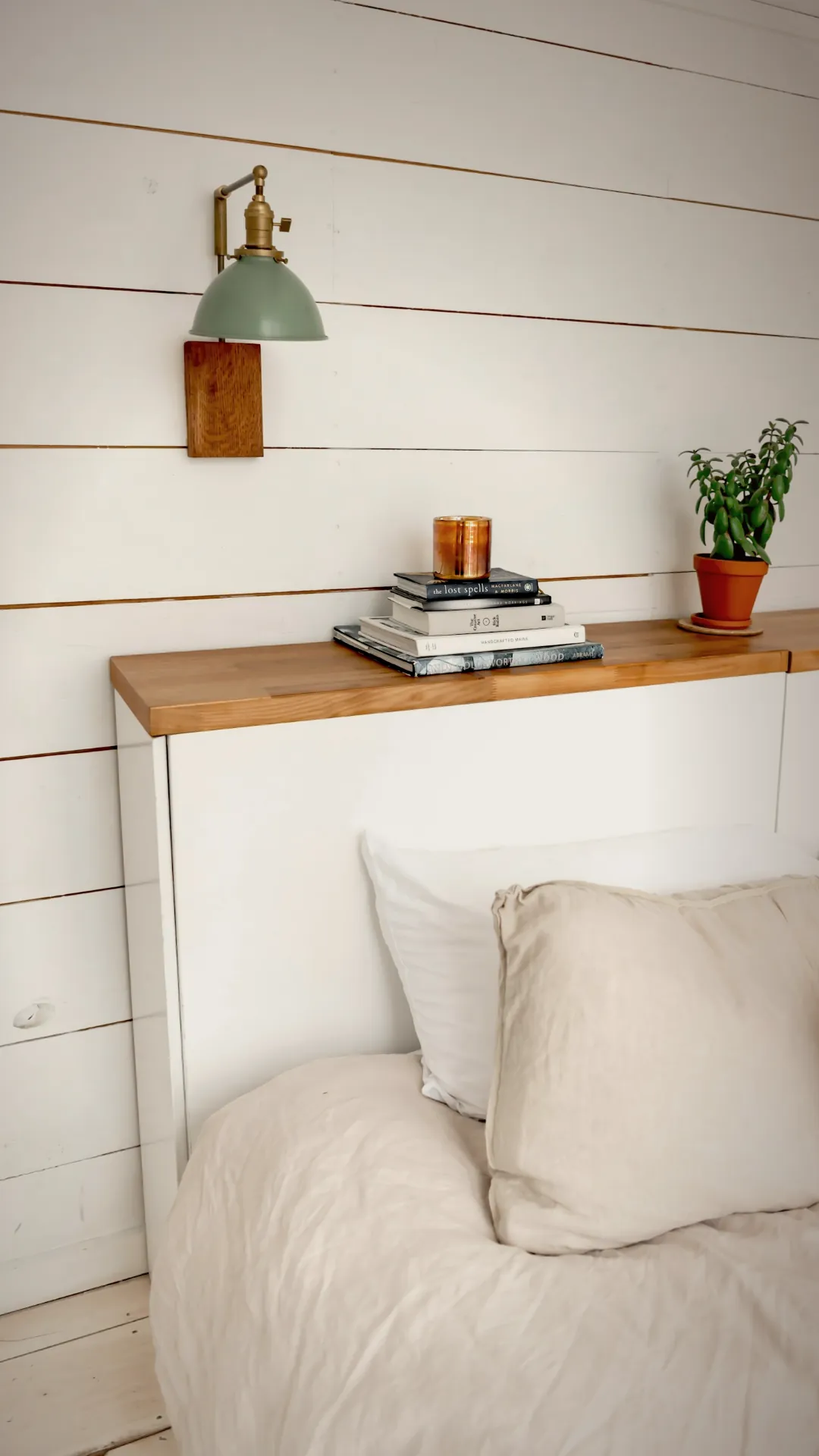 Swing arm wall sconce above a linen headboard angled down onto an open book on the duvet