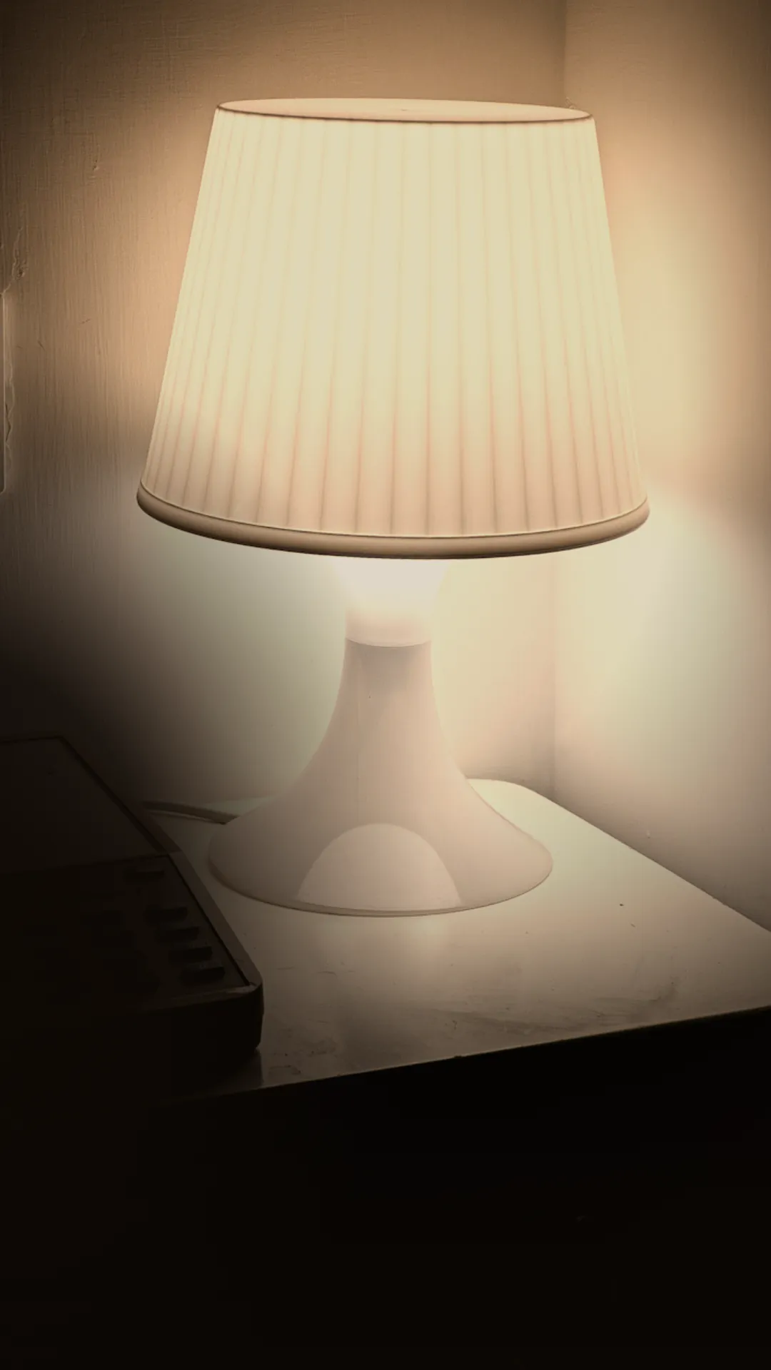 Close up of a warm dimmable LED bulb inside a linen lamp shade on a walnut nightstand with a paperback