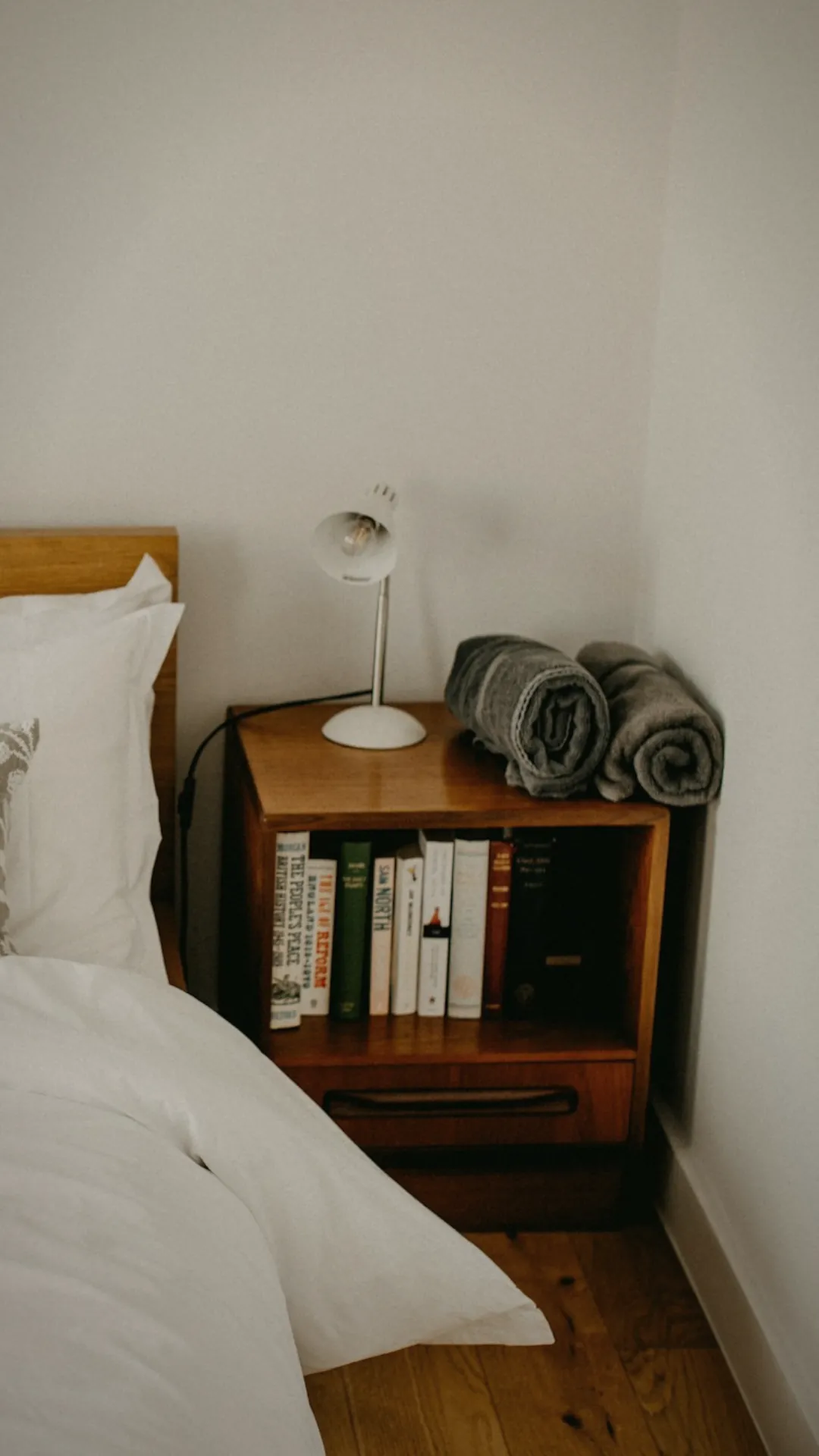 Cozy bedtime reading setup with a reading wedge pillow, nightstand tray holding glasses and water, and a basket of books by the bed